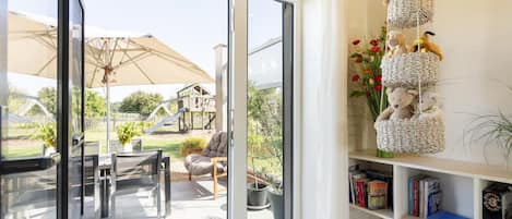 A modern interior with a sliding glass door leading to a patio area, a bookshelf with books, and a hanging basket with stuffed animals.