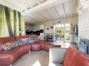 Un interior modern amb un sofà de cuir corbat, un butacó blanc i una porta de vidre que dona a una zona exterior.