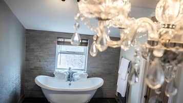 A bathroom with a freestanding bathtub, a window, and a chandelier.