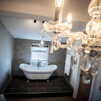 A bathroom with a freestanding bathtub, a window, and a chandelier.