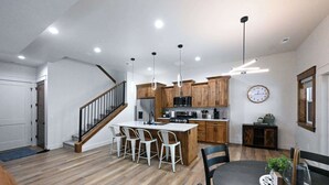 Una cucina moderna con mobili in legno, un'isola centrale con sgabelli da bar, un tavolo da pranzo con sedie e una scala.