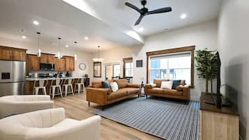 A modern kitchen with a dining area, two sofas, a ceiling fan, and a large window.