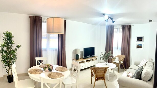 A modern living room with a round dining table, white chairs, a sofa, a TV, and a ceiling fan.