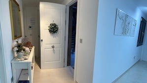 A hallway with a white door, a small desk with a vase of flowers, and a staircase leading to another room.
