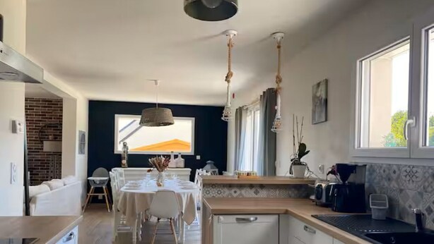 Et moderne køkken med hvide skabe, en indbygget opvaskemaskine og et spiseområde med bord og stole.