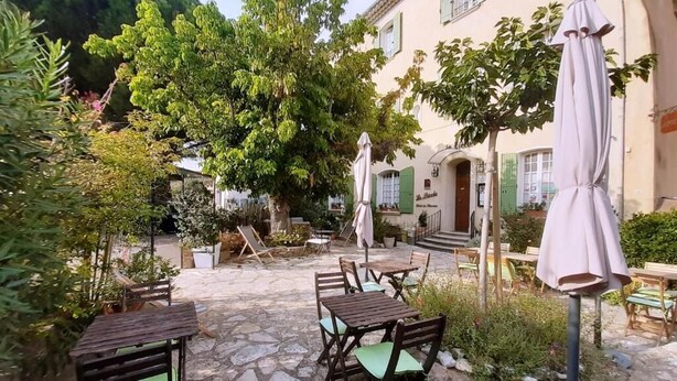 Un patio al aire libre con suelo de piedra, mesas y sillas de madera, y sombrillas.