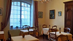 Un comedor con mesas y sillas de madera, un ventanal con cortinas y cuadros en las paredes.