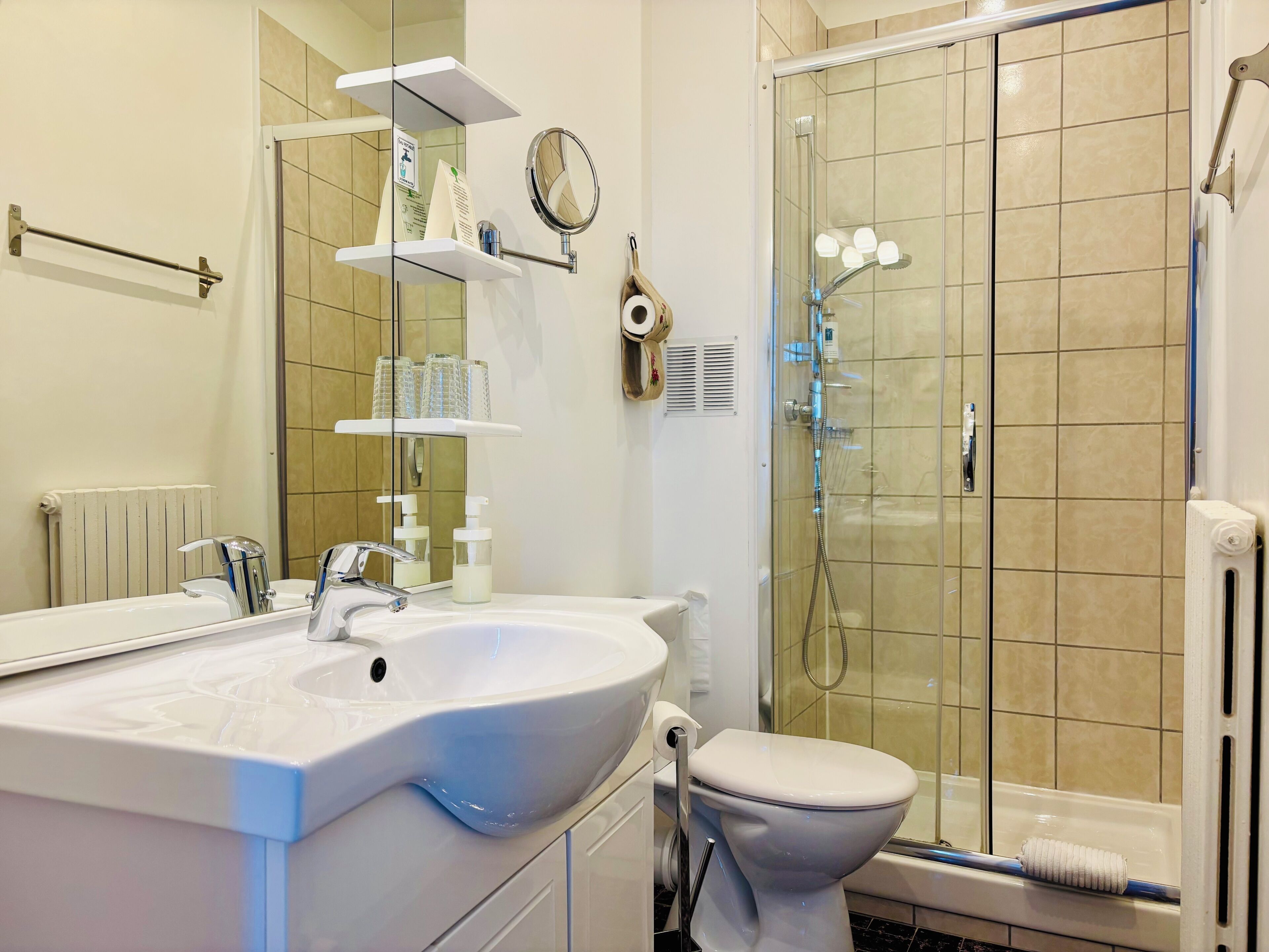 Une salle de bain avec un lavabo blanc, un miroir, des toilettes et une douche séparée par une paroi en verre.