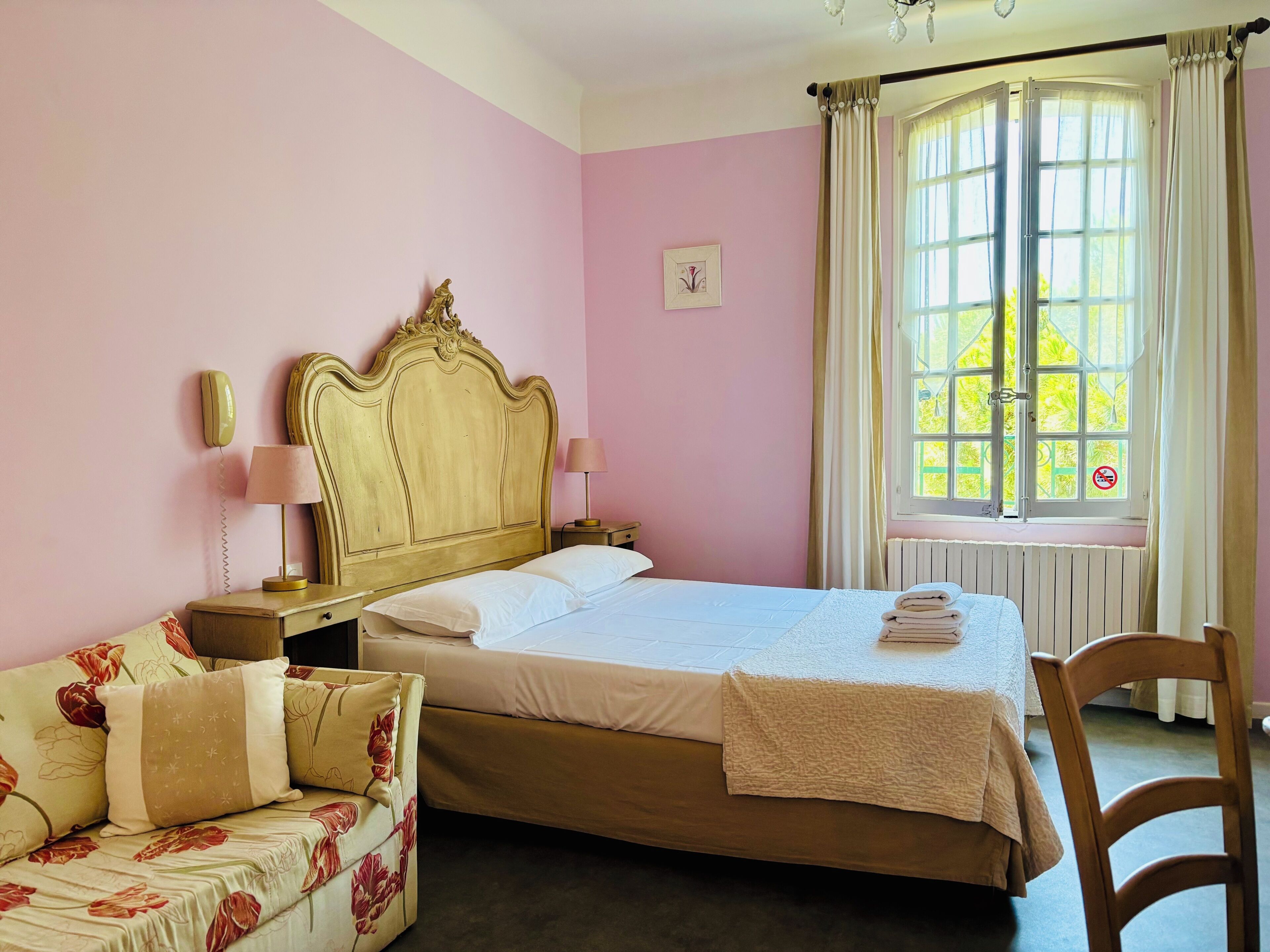 Un dormitorio con cama, mesita de noche, lámpara, silla y ventana con cortinas.