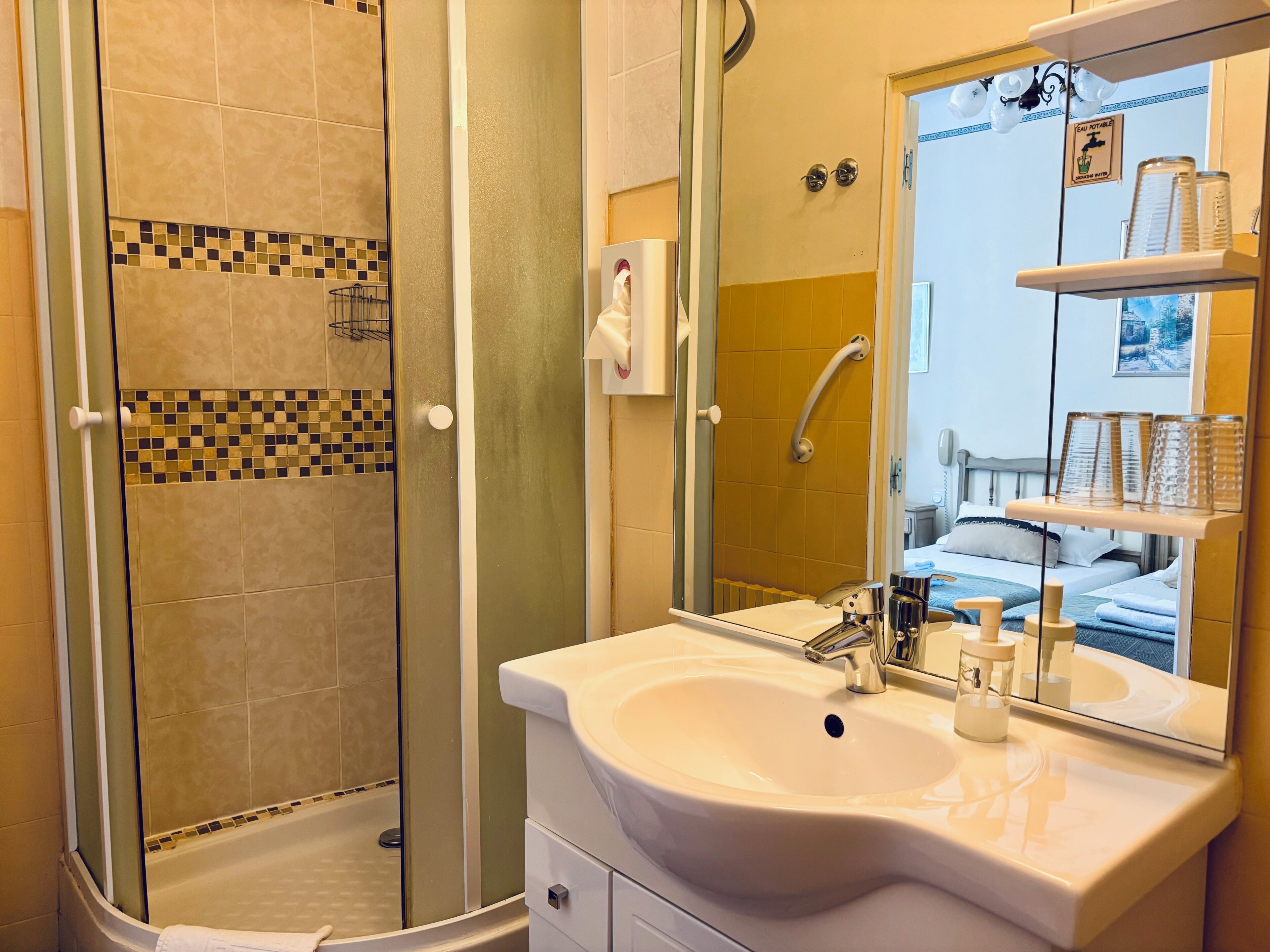 Un baño con cabina de ducha de vidrio, lavamanos con espejo y repisa con artículos de aseo.