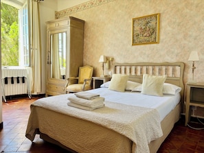 A hotel room with a large bed, a chair, a dresser, a mirror, and a painting on the wall.