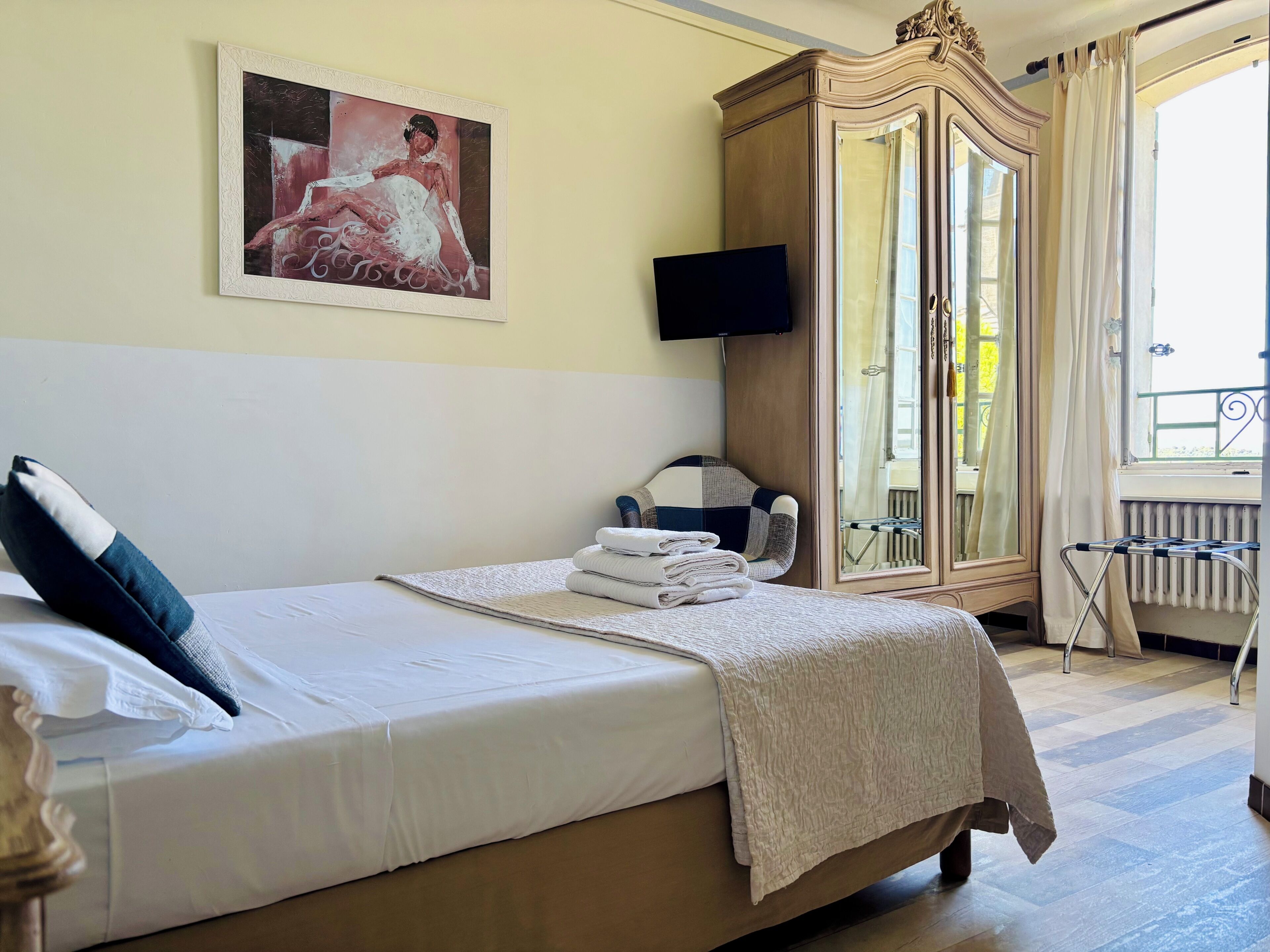Una habitación de hotel con cama, televisión, armario y ventana con cortinas.