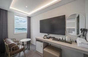 Habitación de hotel con cama, escritorio con televisor de pantalla plana, silla, mesita, espejo y ventana con vistas.
