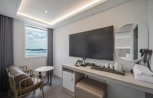 Quarto de hotel com cama, secretária, televisão de tela plana, cadeira, mesa pequena, espelho e janela com vista.