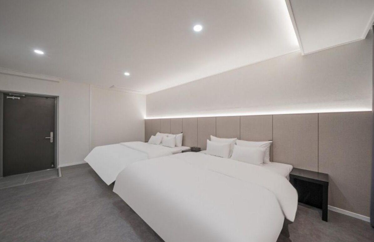 Habitación de hotel moderna con dos camas, una puerta oscura e iluminación empotrada en el techo.