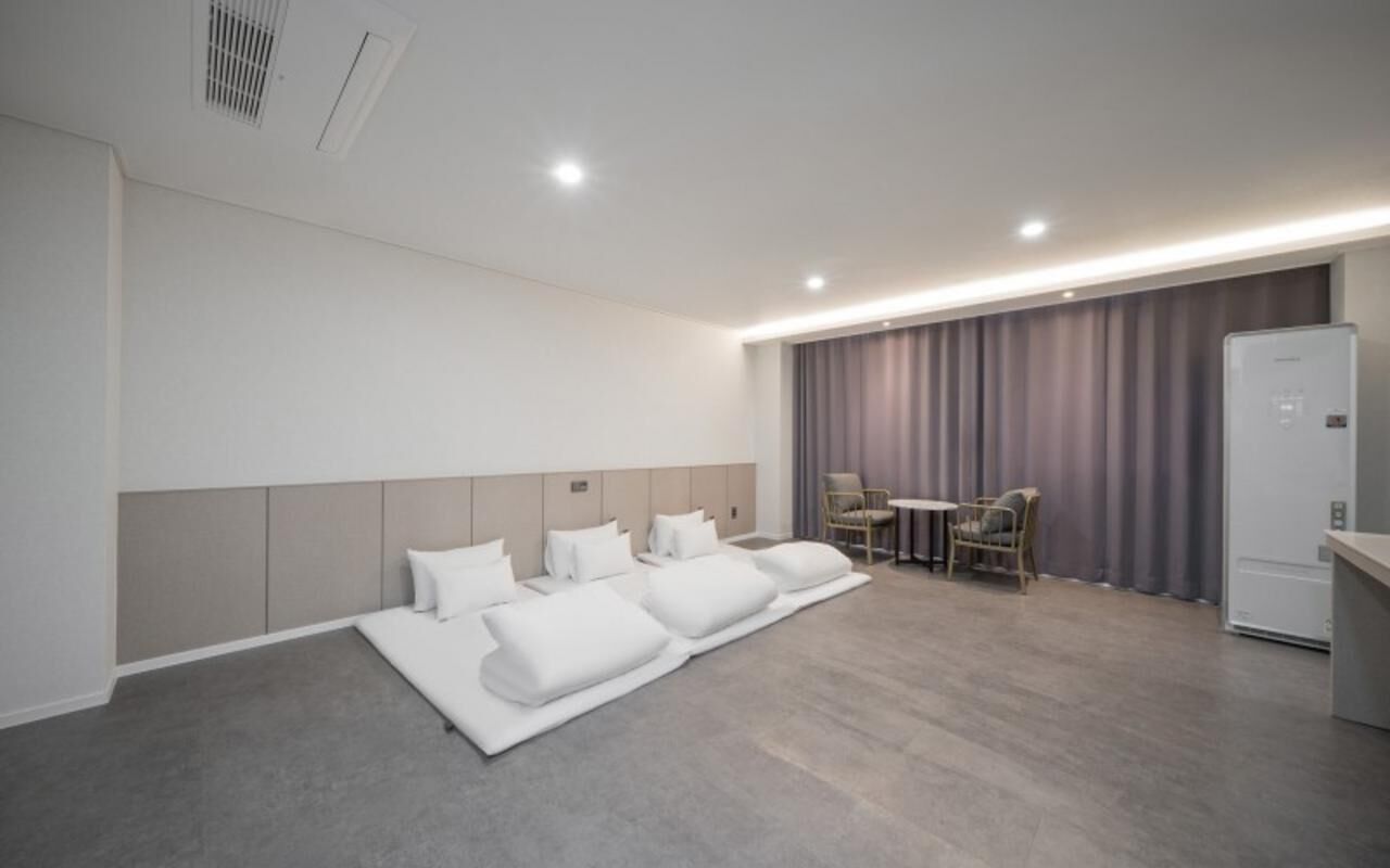 A modern hotel room with a large bed, a small table, chairs, and a refrigerator.
