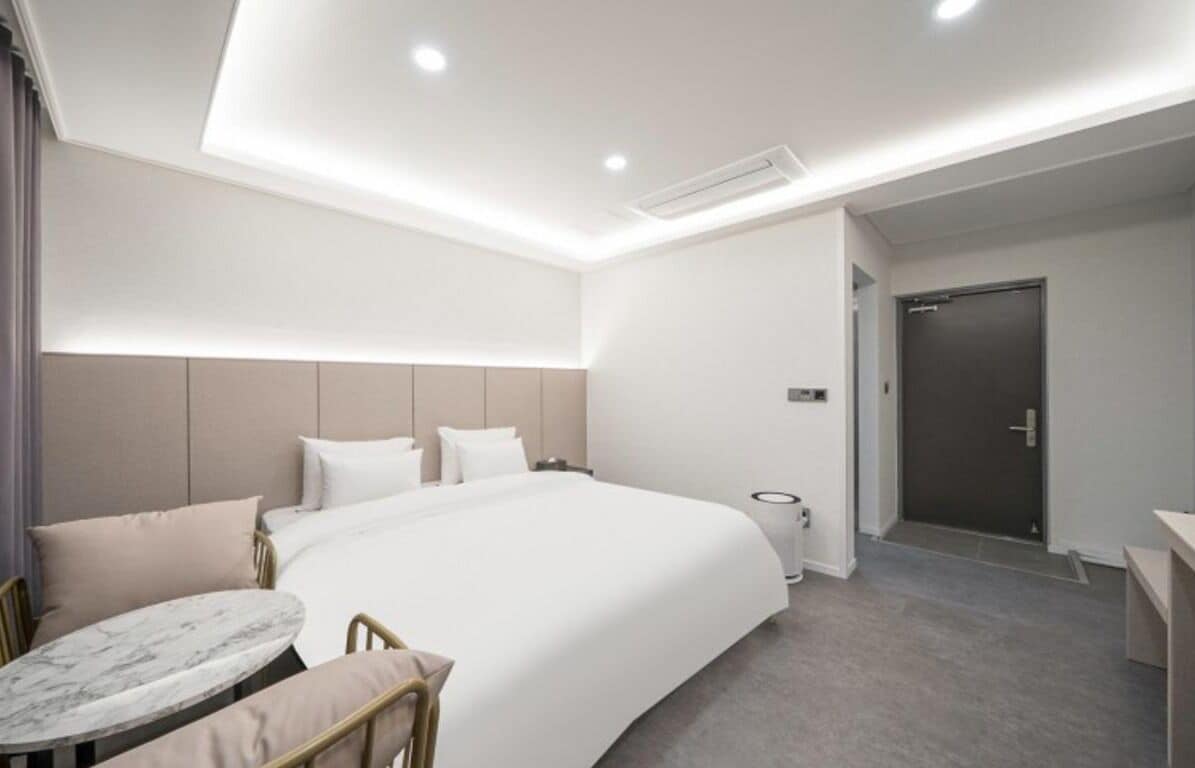 Une chambre d’hôtel moderne avec un grand lit, des tables de chevet, une petite table ronde et une porte.