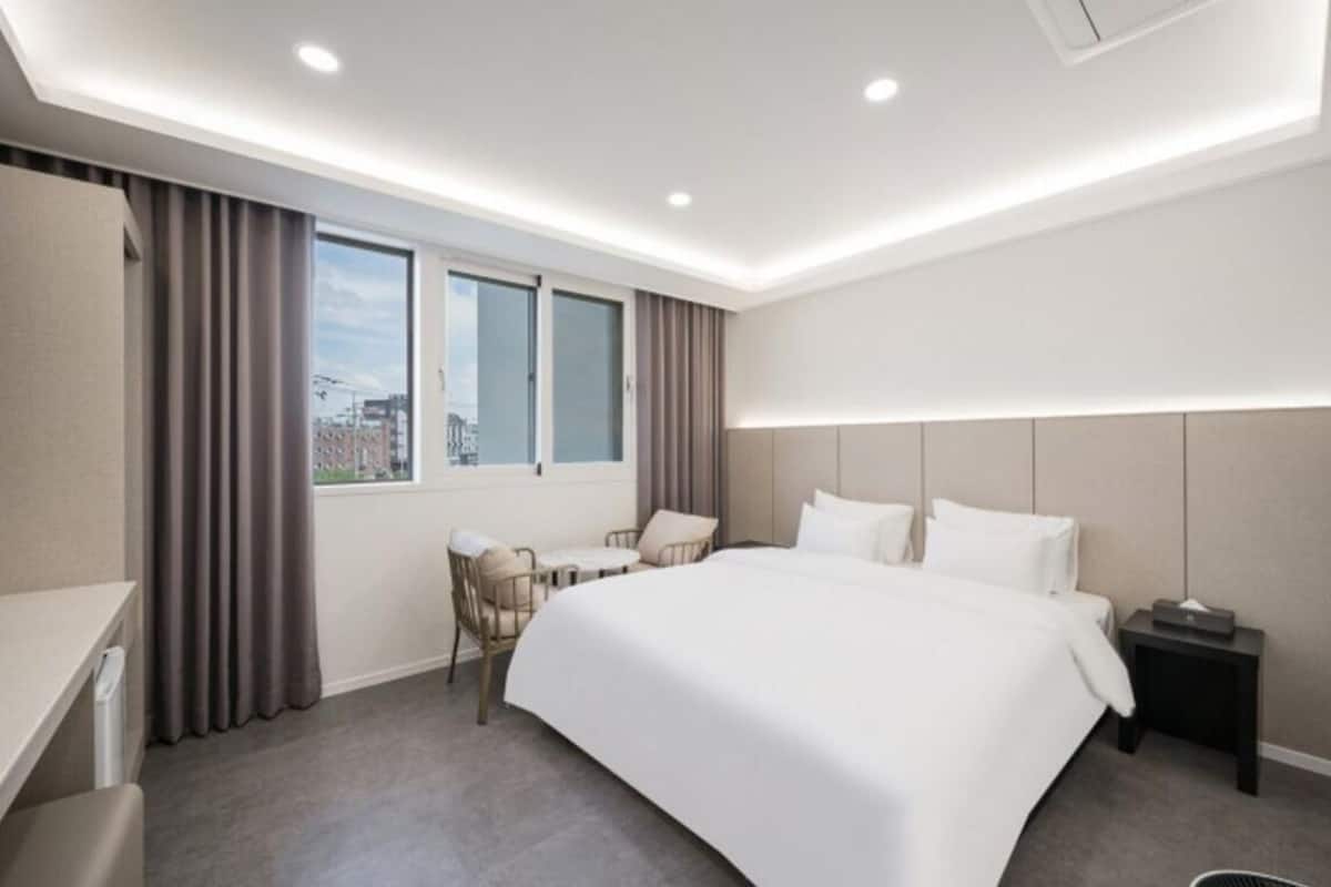 Habitación de hotel con una cama grande, un escritorio, una silla, una ventana con cortinas y una mesita de noche.