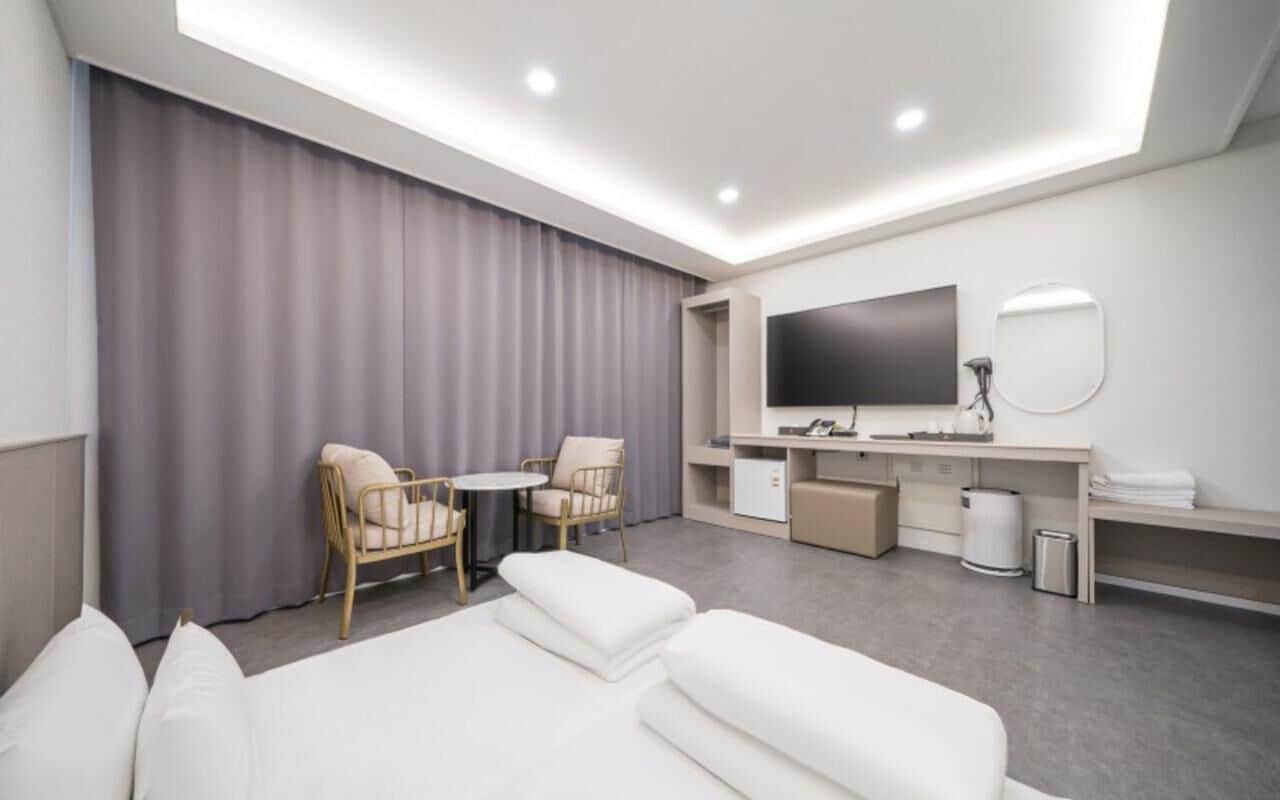 Una habitación de hotel moderna con un sofá, dos sillones, un televisor, un espejo y un escritorio.