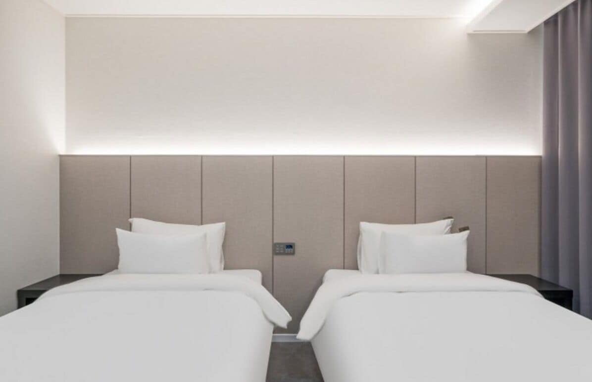 A hotel room with two beds, a headboard, a control panel, and a curtain.