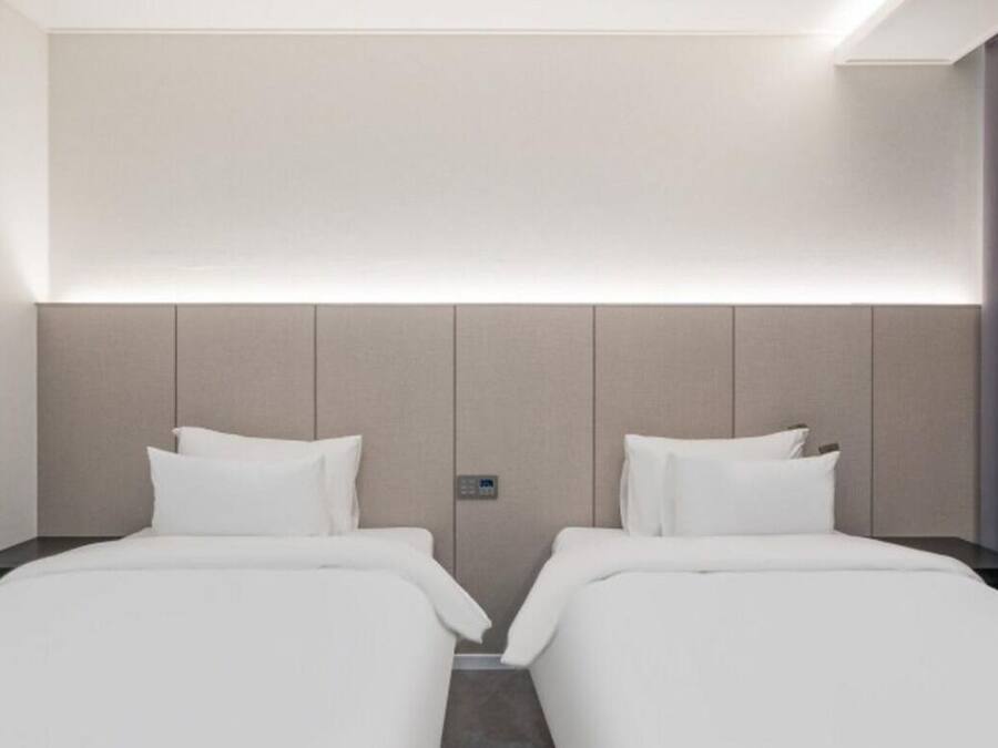 A hotel room with two beds, a headboard, a control panel, and a curtain.