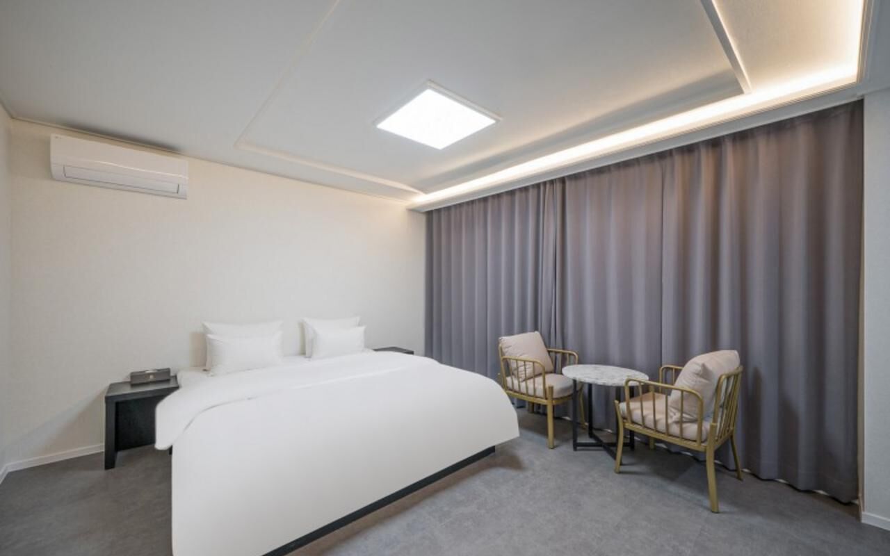 Ein Hotelzimmer mit Bett, Nachttisch, zwei Stühlen, einem kleinen Tisch und einem Fenster mit Vorhängen.