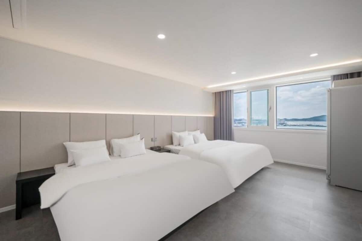 Una habitación de hotel moderna con dos camas, un ventanal con vistas y un refrigerador incorporado.