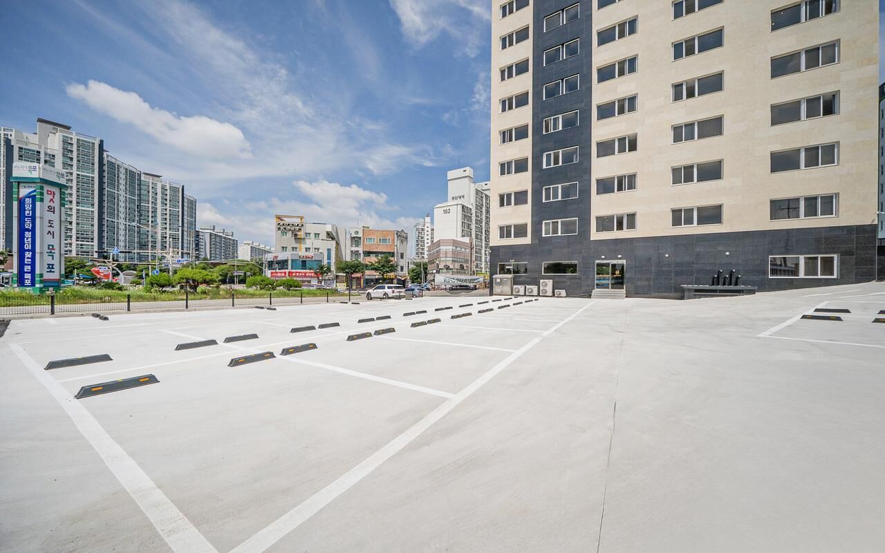 A modern building with multiple floors, a parking area with marked spaces, and a clear sky.