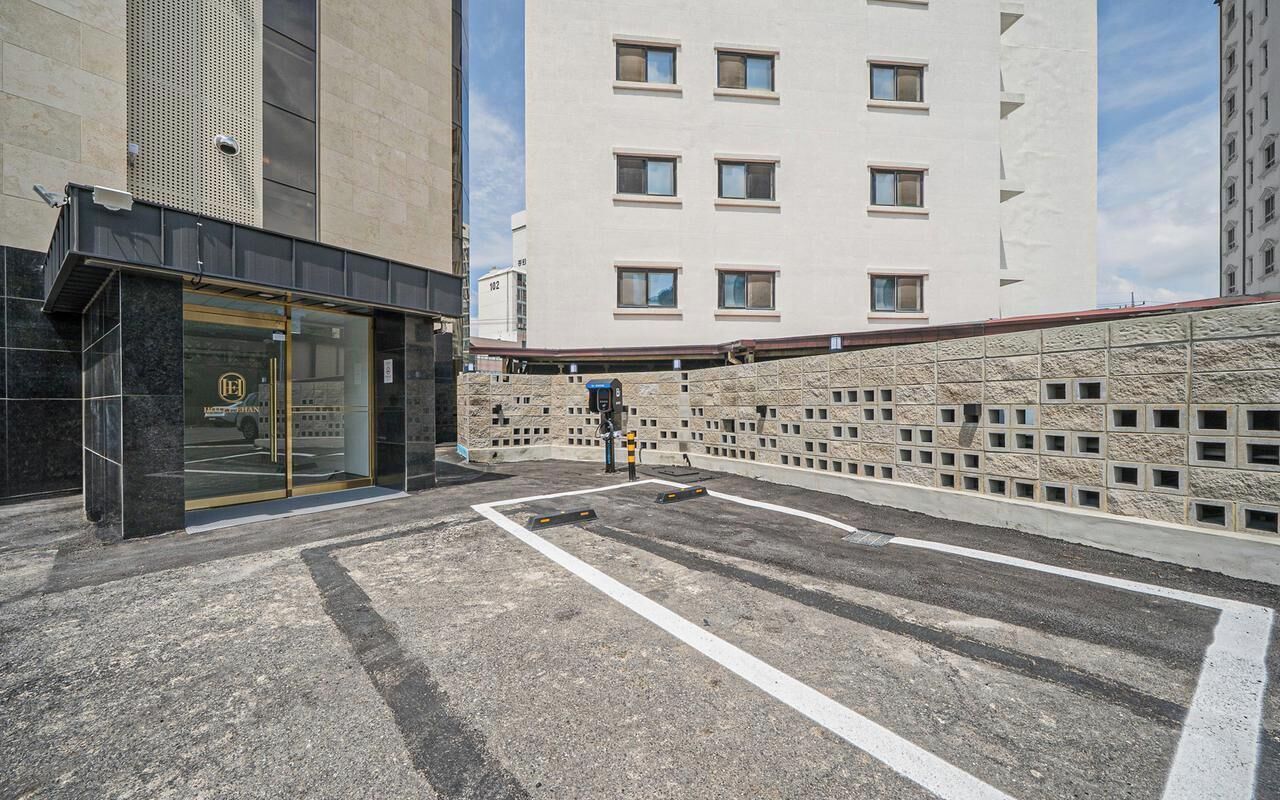 A hotel entrance with a glass door, a parking area, and a building with a stone facade and multiple windows.