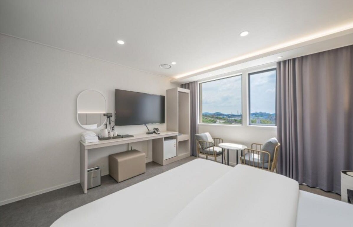 A modern hotel room with a large bed, a desk with a flat-screen TV, a small table, and a chair.