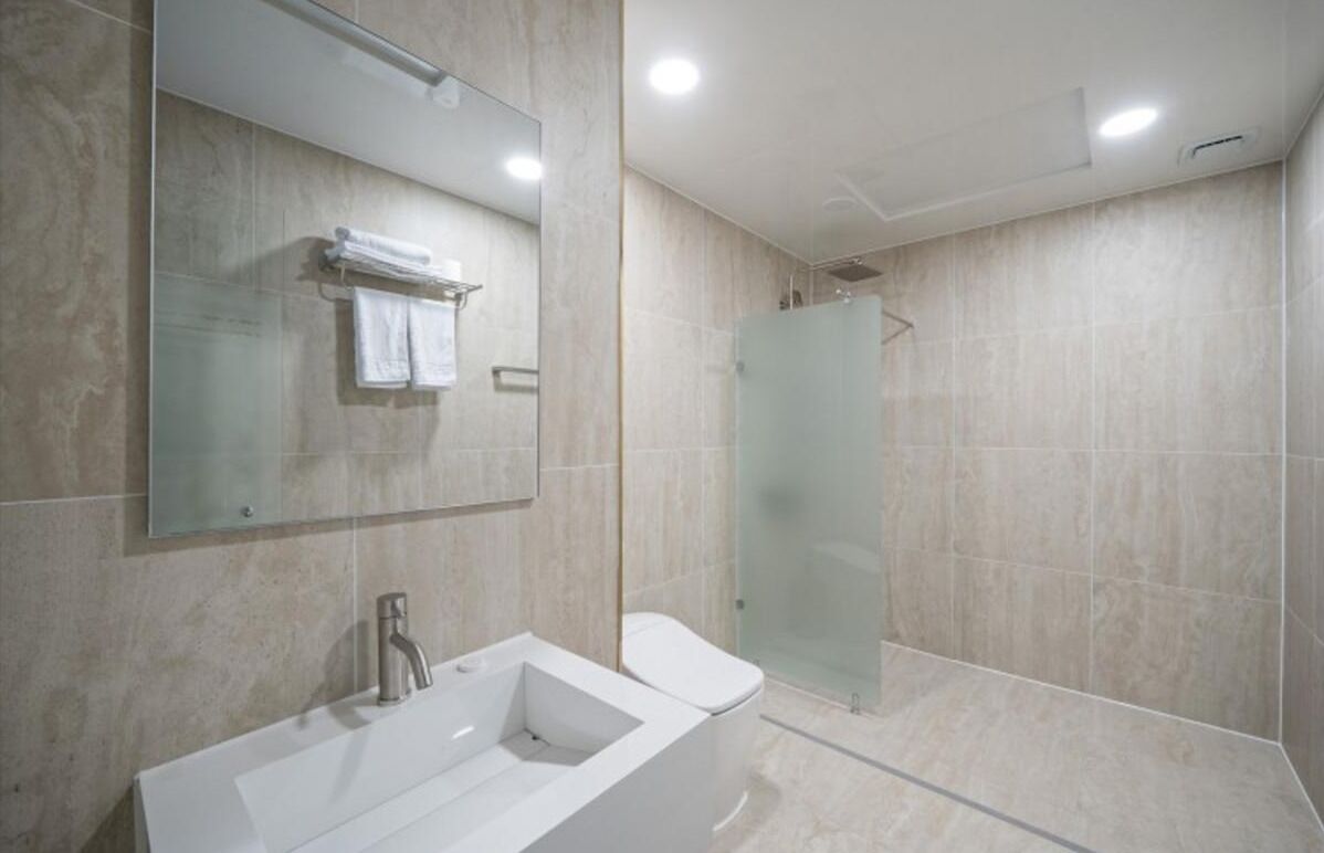 A modern bathroom with a large mirror, a bathtub, a toilet, and a glass shower enclosure.