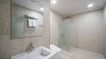 A modern bathroom with a large mirror, a bathtub, a toilet, and a glass shower enclosure.