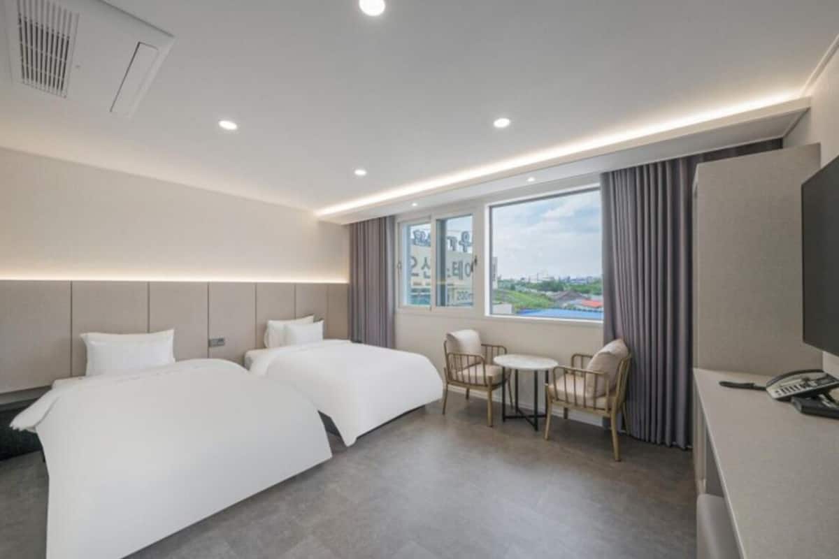 Habitación de hotel con dos camas, un escritorio, una silla y una ventana con vistas.