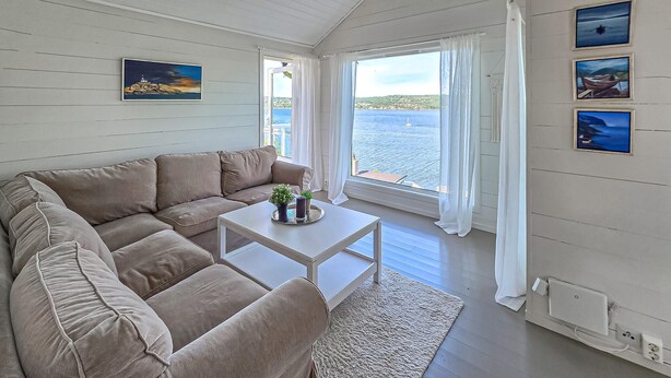 Une pièce chaleureuse avec un canapé beige, une petite table agrémentée d’une plante et une vue sur la mer grâce à de grandes fenêtres.