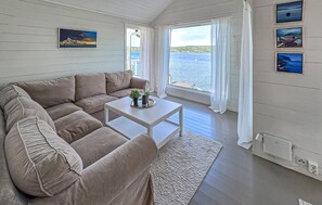 Quarto aconchegante com um sofá bege, uma mesinha com uma planta e vista para o mar através de grandes janelas.