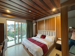 Quarto com uma cama grande, vista para área externa por uma porta deslizante e teto de madeira.