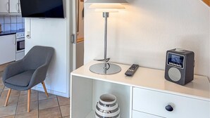 Una habitación moderna con televisión de pantalla plana, una lámpara, un radio, una silla y una mesita.