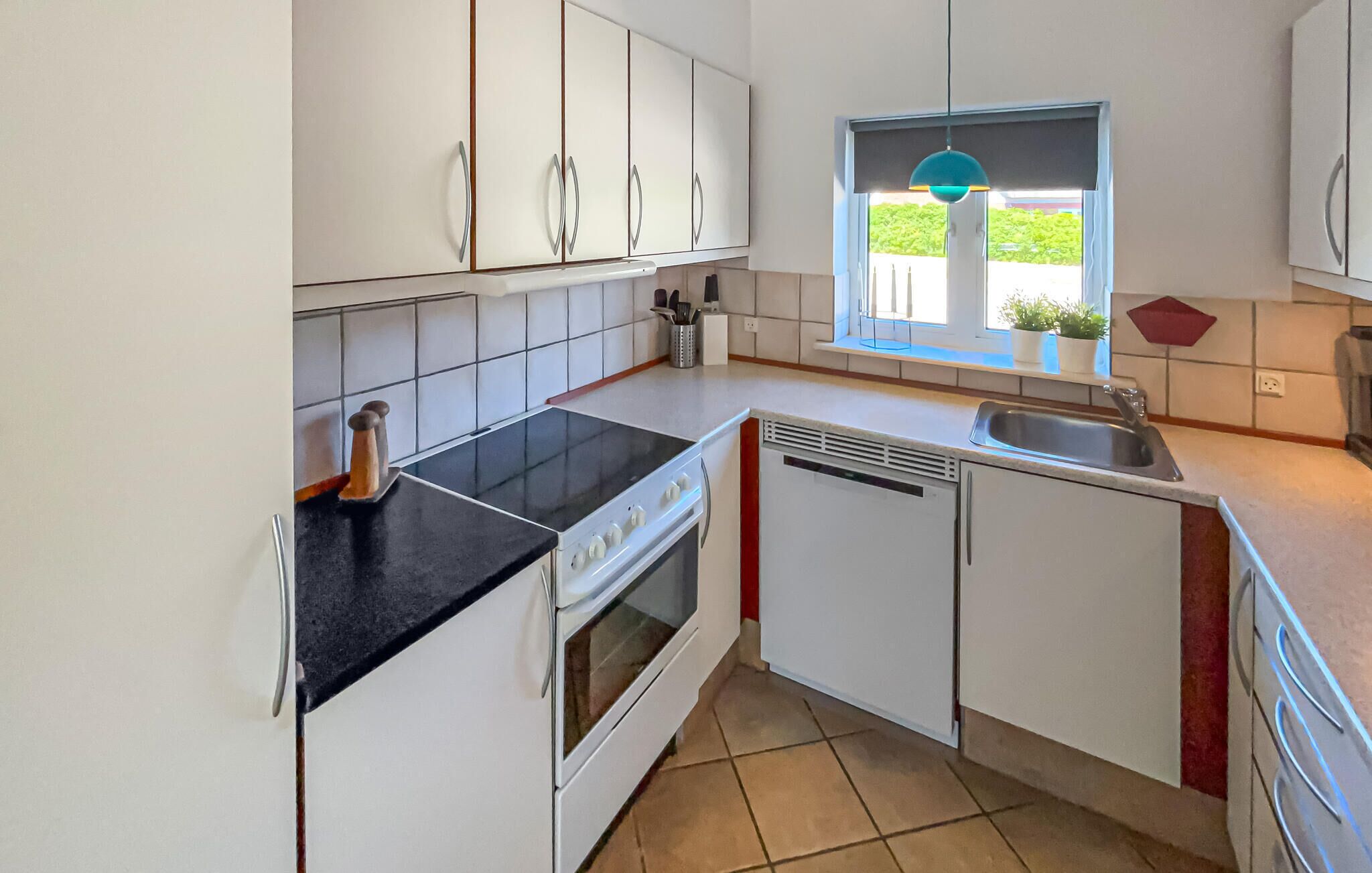 A compact kitchen with white cabinets, a black countertop, a stove, a dishwasher, and a window with a view of greenery.