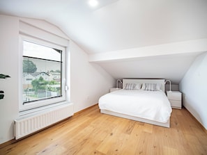 A bedroom with a sloped ceiling, a bed with white bedding, a bedside table, and a window with blinds.