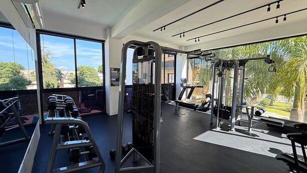 A gym with exercise equipment, large windows, and a view of greenery. - Boho Luxury Stay•Pool•Gym/Near Everything (Santiago de los Caballeros)