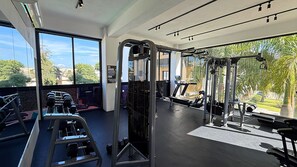 A gym with exercise equipment, large windows, and a view of greenery. - Boho Luxury Stay•Pool•Gym/Near Everything (Santiago de los Caballeros)
