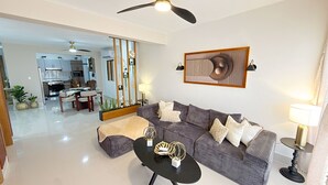 A modern living room with a sofa, coffee table, and decorative items. There is a dining area in the background with a kitchen visible. - Boho Luxury Stay•Pool•Gym/Near Everything (Santiago de los Caballeros)