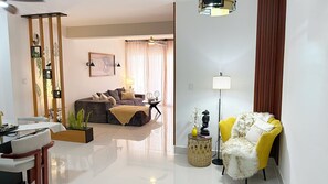 Uma sala de estar moderna com um sofá, uma poltrona amarela, uma mesa de jantar e um abajur.