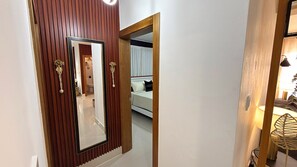 A hallway with a wooden door and a mirror reflecting a bedroom with a bed and a nightstand. - Boho Luxury Stay•Pool•Gym/Near Everything (Santiago de los Caballeros)