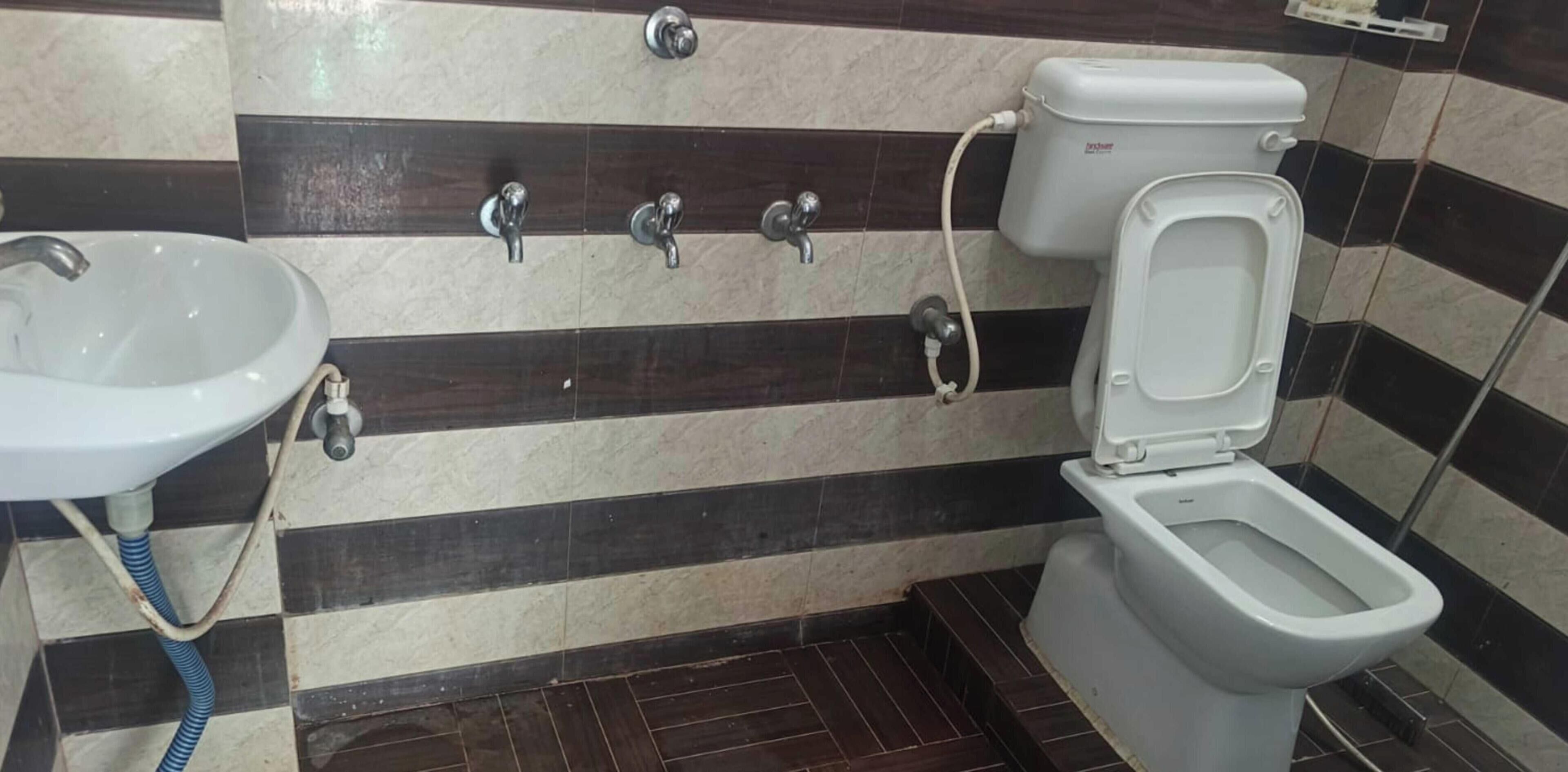 A bathroom with a toilet, sink, and three faucets on the wall.
