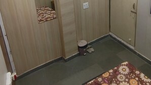A room with a bed, an air conditioning unit, a ceiling fan, a door, and a small stool.
