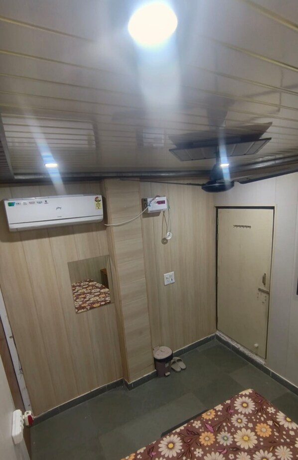A room with a bed, an air conditioning unit, a ceiling fan, a door, and a small stool.