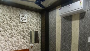 A bedroom with a bed, a wooden nightstand, a ceiling fan, an air conditioning unit, and a small table.