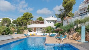 A swimming pool with lounge chairs and umbrellas, surrounded by buildings and trees. - Apartment Playa Dor 27 in first sea line, Cala Gran beach (Cala D'or (Santanyí))