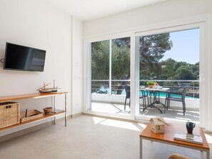 Ein modernes Zimmer mit Fernseher, einem Holztisch, einem Korbschrank und Blick auf einen Pool und Bäume.